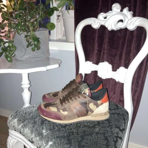Byten sökes  - Snygga sneakers från Valentino med ett coolt camouflage-mönster i bruna och beige toner. Skorna har detaljer i rött och orange samt en bekväm sula. Perfekta för dig som vill sticka ut med stil!