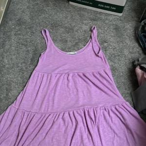 Lila klänning från Pull&Bear - Säljer en söt lila klänning från Pull&Bear i storlek XS. Klänningen har en avslappnad passform med breda axelband och ett ribbat mönster. Perfekt för varma dagar!