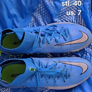 Blå Nike Phantom GT fotbollsskor  - Snygga blå Nike Phantom fotbollsskor med snörning och en modern design. Skorna har en strömlinjeformad form med svarta och silverfärgade detaljer. Perfekta för fotbollsplanen med en tight passform för optimal kontroll. OBS!! påse ingår!