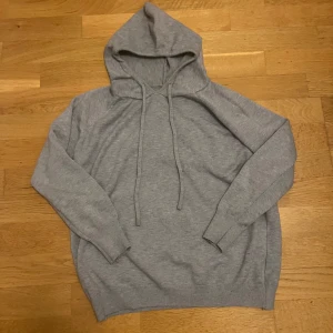 Merinoull hoodie - Säljer en stilren grå hoodie med långa ärmar och ribbade muddar. Perfekt för en avslappnad look. Den har en klassisk huva med dragsko för justering. Passar bra till både jeans och mjukisbyxor.