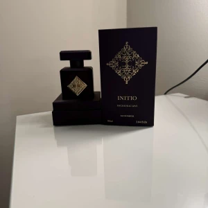Initio Psychedelic Love Eau de Parfum - Exklusiv parfym från Initio, Psychedelic Love, i en elegant mörklila flaska med gulddetaljer. Flaskan rymmer 90 ml och har en lyxig design med ett dekorativt mönster på framsidan. Perfekt för den som söker en unik och sofistikerad doftupplevelse.