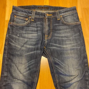 Blå jeans från Nudie Jeans - Snygga blå jeans från Nudie Jeans med klassisk femficksdesign och kontrastsömmar. De har en normal passform och är tillverkade i slitstarkt denim. Perfekta för en avslappnad stil.