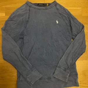 Polo Ralph lauren tröja - Säljer en stilren blå långärmad tröja från Polo Ralph Lauren med det klassiska broderade logotypen på bröstet. Perfekt för en avslappnad look. Tröjan har ribbade muddar vid ärmslut och nederkant. Den är i bra skick!😊