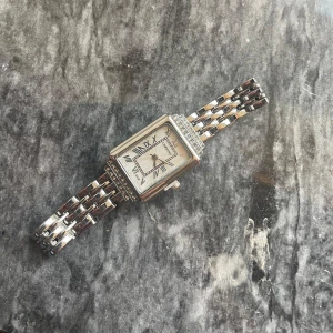 Elegant rektangulär klocka med länkarmband - Snygg klocka med rektangulär urtavla och romerska siffror. Klockan har ett silverfärgat länkarmband och detaljer runt urtavlan som ger en lyxig känsla. Perfekt för den som gillar stilrena accessoarer. Säljer för den är väldigt stor för mig och jag har inga verktyg för att fixa det.