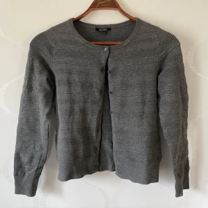 Grå kofta från Esmara - Säljer en stilren grå kofta från Esmara. Den har en rund halsringning och knappar framtill. Perfekt för lager-på-lager under kyligare dagar. Koftan har en diskret ribbad struktur som ger den en extra touch.