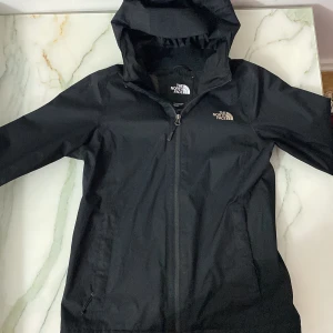 Svart regnjacka från The North Face - Säljer en svart regnjacka från The North Face med huva och dragkedja. Jackan har en meshfoder på insidan för extra komfort. Perfekt för regniga dagar och håller dig torr och bekväm. 🖤