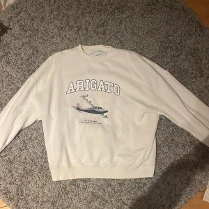 Vit sweatshirt från Axel Arigato - Säljer en stilren vit sweatshirt från Axel Arigato med ett tryck av ett flygplan och texten 'Arigato' på framsidan. Perfekt för en avslappnad look. Tröjan har långa ärmar och en rund halsringning. Nypris 2200 limited edition 