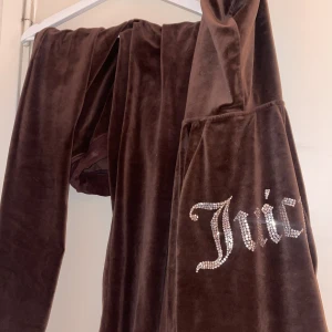 Brun velourjacka från Juicy Couture - Säljer en brun velourjacka och byxor  från Juicy Couture med diamanter. Jackan har en mjuk och lyxig känsla, perfekt för en avslappnad stil. Använt 2-3 ggr och säljer för jag använder inte längre, byxorna är strl xs och koftan är M. Jag är 158 och dom är lite långa för mig. Koftan passar bra. Säljer helt nytvättad. Inga fläckar eller hål!💕💕säljer byxorna för 650 och tröjan för 500