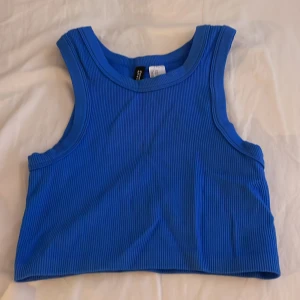 Blå ribbad linnetopp från H&M Divided - Säljer en snygg blå ribbad linnetopp från H&M Divided. Perfekt för varma dagar eller som ett lager under en jacka. Toppen är ärmlös och har en croppad passform. Ett måste i garderoben för en stilren look!