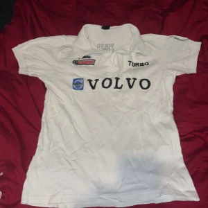 Vit kortärmad t-shirt från Volvo - Säljer en vit kortärmad t-shirt från Volvo med tryck av 'Volvo Turbo' och 'Volvo Racing'. T-shirten har en klassisk krage och är perfekt för bilentusiaster. Den har även broderade detaljer på ärmen.