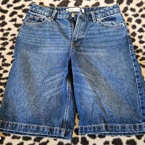 Blå jeansshorts - Säljer ett par klassiska blå jeansshorts med fem fickor och knappgylf. Perfekta för en avslappnad stil. De har en normal passform och är knälånga.