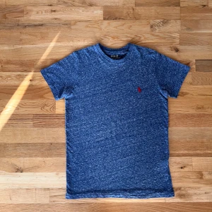 Blå t-shirt från Ralph Lauren - Snygg blåmelerad t-shirt från Ralph Lauren med det klassiska röda broderade logotypen på bröstet. T-shirten har en normal passform och är kortärmad, perfekt för en avslappnad stil.