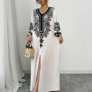 Abaya - Elegant vit långklänning med svart broderi och v-ringad hals. Klänningen har trekvartsärmar och en slits framtill som ger en stilfull touch. Perfekt för speciella tillfällen.