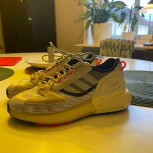 Adidas sneakers med grå och röda detaljer - Snygga Adidas sneakers i grått med röda och svarta detaljer. Sparsamt använda då d r lite små för mig tyvärr