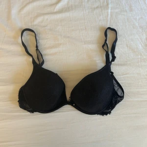 Svart spets-bh med vadderade kupor - Säljer en svart bh med vadderade kupor och fina spetsdetaljer på sidorna. Axelbanden är justerbara och bh:n har hakknäppning bak. 