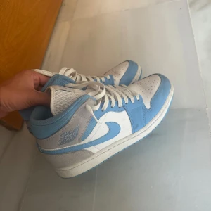 Nike Air Jordan 1 Mid University Blue - Säljer ett par Nike Air Jordan 1 Mid i färgen University Blue. Skorna har en snygg kombination av ljusblått och vitt skinn med klassisk Jordan-logga på sidan och tungan. Perfekta för dig som gillar streetwear och vill sticka ut med en ikonisk sneaker.