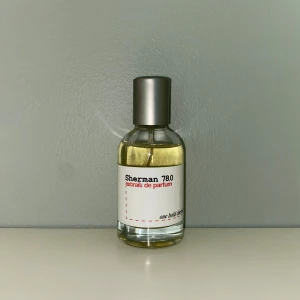 Sherman 780 extrait de parfum - En stilren parfymflaska med silverfärgat lock och transparent glas. Innehåller Sherman 780 extrait de parfum, en exklusiv doft med modern känsla. Flaskan har minimalistisk vit etikett med svart och röd text. Väldigt lik Kilians smoking hot