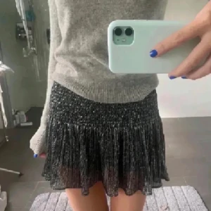 Glittrig svart minikjol - Supersnygg svart minikjol från zara med glittrigt tyg och volang nertill. Kjolen har resår i midjan och ett lätt plisserat material som ger en cool och trendig look.