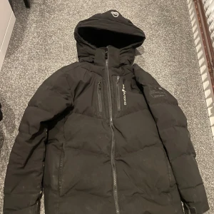 Svart dunjacka med huva - Säljer en svart dunjacka från Sail Racing  med huva och dragkedja. Jackan har små defekter. dragkedjan hat gått sönder på höger fickan samt så hål på undersidan av armarna men inga hål där det kommer ut dun. jackan är också ganska smutsig men efter en tvätt så är den i finare skick. jackan är i storlek xs/160. kan släppa billigare vid snabb affär. alltid snabba svar!