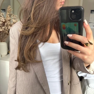 Beige rutig kavaj - Snygg beige kavaj med rutigt mönster och två knappar framtill. Klassisk passform och långärmad modell, perfekt att styla över en t-shirt eller topp. Tidlös design som funkar till många olika looks.