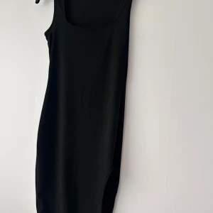 Svart ärmlös långklänning - En stilren svart långklänning med rund halsringning och ärmlös design. Klänningen har en enkel och tidlös form som passar perfekt till många olika tillfällen. Materialet känns mjukt och följsamt mot kroppen.