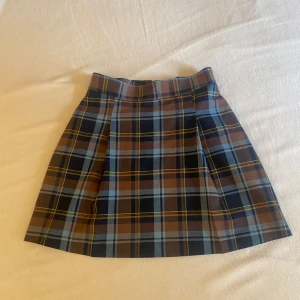 Rutig kjol från M&S Collection - Säljer en snygg rutig kjol från M&S Collection i blått, brunt och gult. Kjolen har en klassisk A-linjeform och dragkedja bak. Perfekt för dig som gillar preppy stil och vill ha något som sticker ut lite extra.