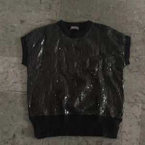 Svart glittrig topp - . Modellen är boxig med korta ärmar och bred mudd nertill. Perfekt för dig som vill sticka ut lite extra.