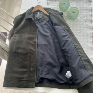 Mörkgrön mockajacka från Dressmann - Säljer en stilren mörkgrön mockajacka från Dressmann. Jackan har dragkedja framtill, klassisk krage och två stora fickor på framsidan. Perfekt för dig som gillar en enkel & classic stil🤩 PS, aldrig använd😁