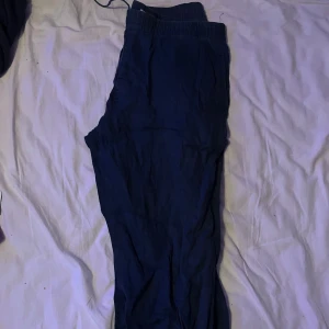 Mörkblå linnebyxor från H&M - Säljer ett par mörkblå linnebyxor från H&M med resår och dragsko i midjan. Byxorna har en avslappnad passform och bakficka. Perfekta för varmare dagar och enkel stil.
