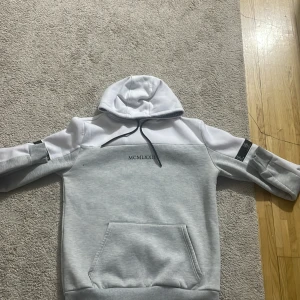 Grå och vit hoodie från Brave Soul - Säljer en stilren hoodie från Brave Soul i grått och vitt. Tröjan har huva med snörning, magficka och svarta detaljer på ärmarna. Perfekt för en avslappnad look.