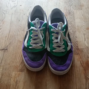 Coola Vans sneakers!! - Säljer ett par Vans sneakers med vit sula och snörning. Skorna har en färgstark design med gröna, lila och svarta paneler samt vit sidoremsa. Klassisk låg modell med rund tå och platt sula. Skokartong följa med. Använda typ 3 gånger 