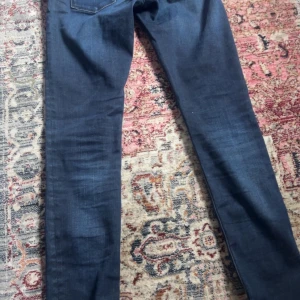 Mörkblå jeansbyxor från Replay New Luz - Säljer ett par mörkblå jeansbyxor från Replay, modell New Luz. Byxorna har klassisk femficksdesign och smal passform. Perfekta till dig som gillar stilrena och tidlösa jeans. Midjemått 27 och längd 32.