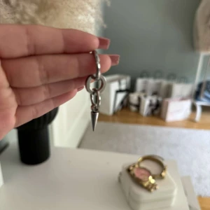 Silvrigt örhänge med spike-detalj - Säljer ett coolt örhänge i silverfärgad metall med två ringar och en hängande spike. Perfekt för dig som gillar edgy och minimalistisk stil.