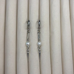 Silverfärgade örhängen med pärldetalj och spetsig hängande berlock - Säljer ett par stilrena silverfärgade örhängen med rund pärldetalj och spetsig, avlång berlock. Perfekta för dig som gillar minimalistisk design med en twist. Passar till många olika stilar.