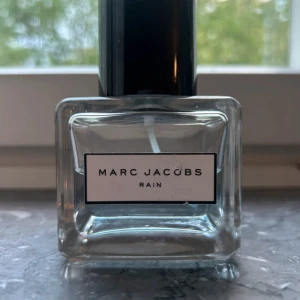 Marc Jacobs Rain Eau de Toilette 100 ml - Fräsch parfym från Marc Jacobs med namnet Rain. Kommer i en stilren, fyrkantig glasflaska med svart lock. Doften är lätt och uppfriskande, perfekt för dig som gillar rena och vattniga toner. Eau de toilette-variant.