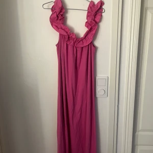 Rosa långklänning med volang - Säljer en rosa långklänning med bred volang runt urringningen. Klänningen har en lös passform, perfekt för varma dagar. Enkel och stilren design som sticker ut med sin färg och volangdetalj. Går både att ha som på bilden men även off shoulder🩷🩷känningen går nästan till fötterna på mig som är 164 cm!
