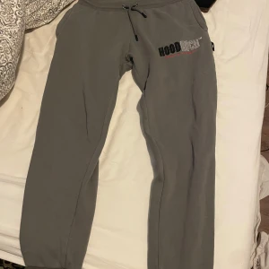 Grå mjukisbyxor från Hoodrich - Säljer ett par grå mjukisbyxor från Hoodrich med logga tryckt på vänster sida. Byxorna har snöre i midjan och muddar vid benen. Perfekta för en avslappnad stil och riktigt sköna att ha på sig.