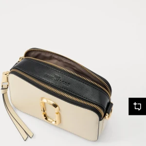  axelväska från Marc Jacobs - Säljer en snygg axelväska från Marc Jacobs i svart och beige med guldfärgade detaljer. Väskan har två fack med dragkedja och en bred, justerbar axelrem med logotyp. Notera att bandet man får med inte ser ut som på bilden. Skriv DM för egna bilder. Väskan är använd ca 5 gånger.