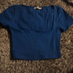 Blå croppad topp från Zara - Säljer en blå croppad topp från Zara med korta ärmar och fyrkantig ringning. Enkel och stilren design som passar perfekt till jeans eller kjol. Supersnygg färg och skön bomullskvalitet!