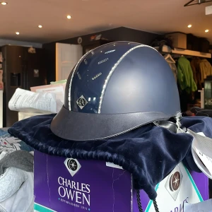 Charles Owen ridhjälm  - Snygg marinblå ridhjälm från Charles Owen med glittriga kristalldetaljer längs ventilationsspåren. Hjälmen har en klassisk form med skärm och är perfekt för ridning. Märket syns framtill och materialet är en blandning av syntet och skinn. Nypris är 8000kr (7999), den är aldrig använd bara testad jag köpte idag men hittade en annan billigare jag hellre vill ha så kollar intresset på denna innan jag bestämt mig.