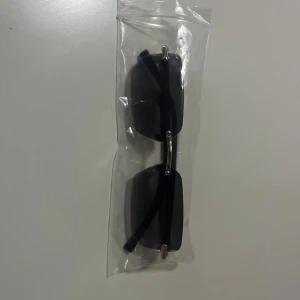 Rektangulära solglasögon med gulddetaljer - Snygga rektangulära solglasögon med svarta bågar och guldfärgade detaljer. Finns i flera färger på glasen: svart, blå och bruntonade. Perfekt accessoar för att lyfta din stil. Glasögonen är helt nya och inte använda köpte dom för betydligt mycket mer pengar men dom ligger bara här hemma så vill göra mig av med dom 85kr styck