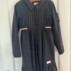 Mörkblå kappa från Odd Molly - Figrursydd mörkblå kappa från Odd Molly med volang nertill samt ljusrosa detaljer. 