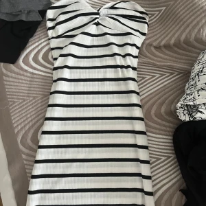 Vit och svart randig ribbad långklänning - Säljer en vit långklänning med svarta horisontella ränder. Klänningen är ribbad, tight och har en snygg v-ringning framtill. Ärmlös modell som sitter figurnära och passar perfekt till sommaren.