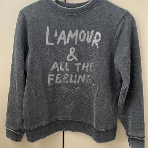 Svart sweatshirt med texttryck - Mysig svart sweatshirt med texten 'L'AMOUR & ALL THE FEELINGS' i vitt framtill. Tröjan har rund halsringning och långa ärmar. Perfekt för en avslappnad stil.