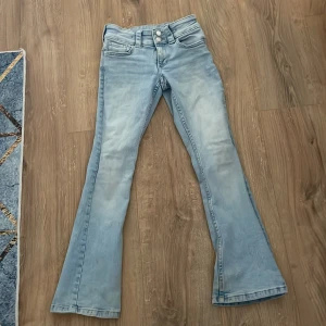 Ljusblå bootcut jeans från Denim - Säljer ett par ljusblå bootcut jeans från H&M med dubbla knappar i midjan och fickor med lock bak. Jeansen har klassisk femficksdesign och är tillverkade i ett mjukt jeanstyg. Perfekta för dig som gillar en retroinspirerad look.