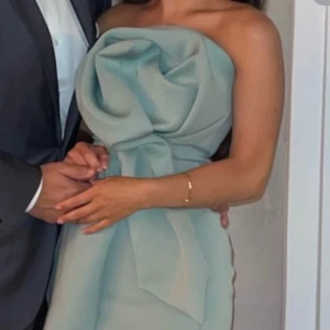 Ljusgrön axelbandslös kortklänning med stor rosett - Superfin axelbandslös klänning i ljusgrönt med en stor dekorativ rosett framtill. Klänningen är kort och har en figurnära passform, perfekt för speciella tillfällen. Materialet ser ut att vara slätt och elegant. 