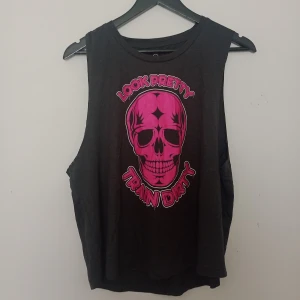 Svart ärmlös linnetopp med tryck - Cool svart ärmlös linnetopp från Northern Spirit med stort rosa döskalle-tryck och texten 'Look Pretty Train Dirty' på framsidan. Tillverkad i en mjuk blandning av polyester och viskos, perfekt för träning eller gym.