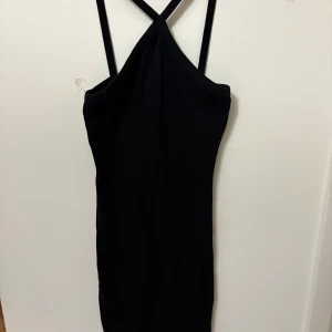 Svart ribbad klänning med smala axelband från 157 - Säljer en svart ribbad klänning från 157 med smala axelband som korsas i ryggen. Klänningen är tight och har en enkel, stilren design som passar perfekt till sommaren.