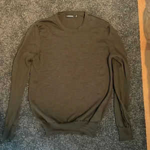 Olivgrön stickad tröja från J.Lindeberg - Säljer en stilren olivgrön stickad tröja från J.Lindeberg. Tröjan har rund halsringning, långa ärmar och diskret broderad logga på bröstet. Perfekt för lager-på-lager och passar till många olika outfits.