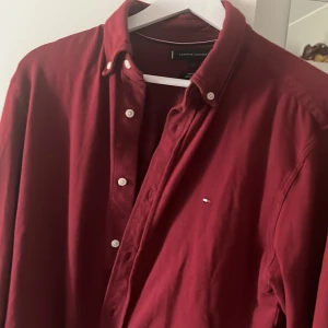 Vinröd skjorta från Tommy Hilfiger - Säljer en vinröd långärmad skjorta från Tommy Hilfiger i regular fit. Skjortan har klassisk krage, knappar framtill och liten broderad logga på bröstet. Perfekt för dig som gillar stilrena plagg med snygga detaljer. Skriv gärna vid frågor😊👍